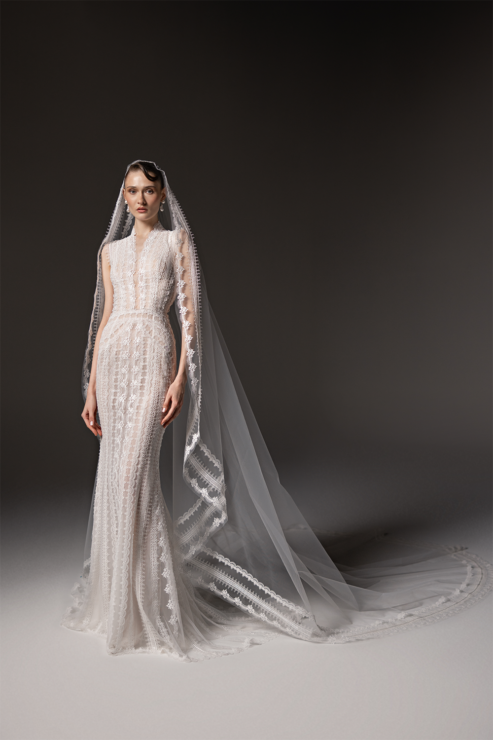 High-neck sleeveless bridal gown in delicate patterned lace with a fitted silhouette and a long lace-trimmed tulle veil.