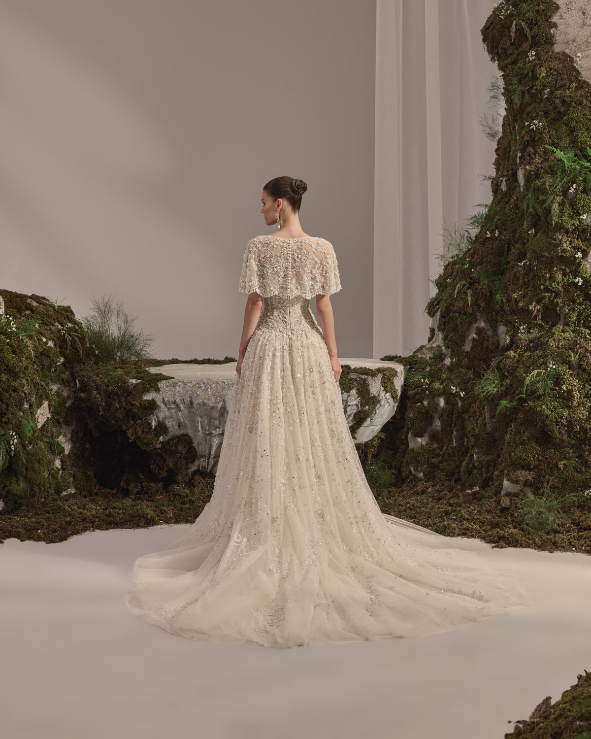 Bridal gown with a bateau neckline, short embellished sleeves, intricately embroidered bodice, fitted waist and flowing beaded tulle skirt with train.