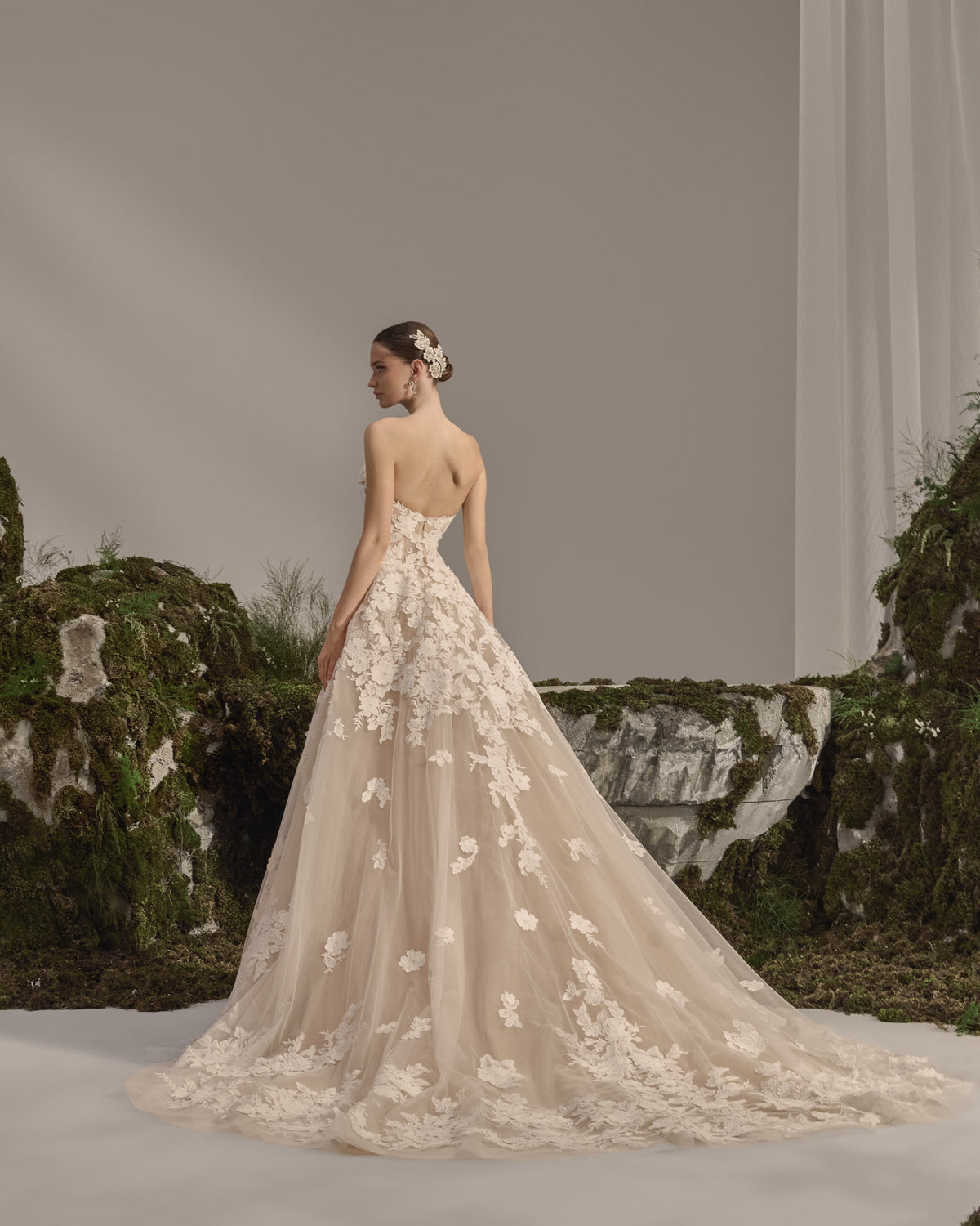 Strapless bridal gown with floral lace appliqués, sculpted fitted silhouette and a flowing lace overskirt.