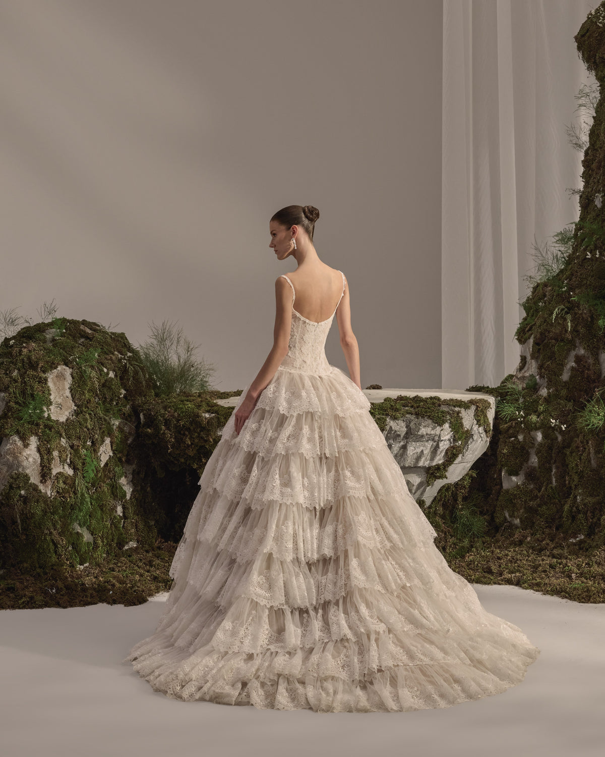 Bridal gown with a fitted lace corset bodice, delicate straps, button detailing, voluminous tiered lace skirt and sheer veil.