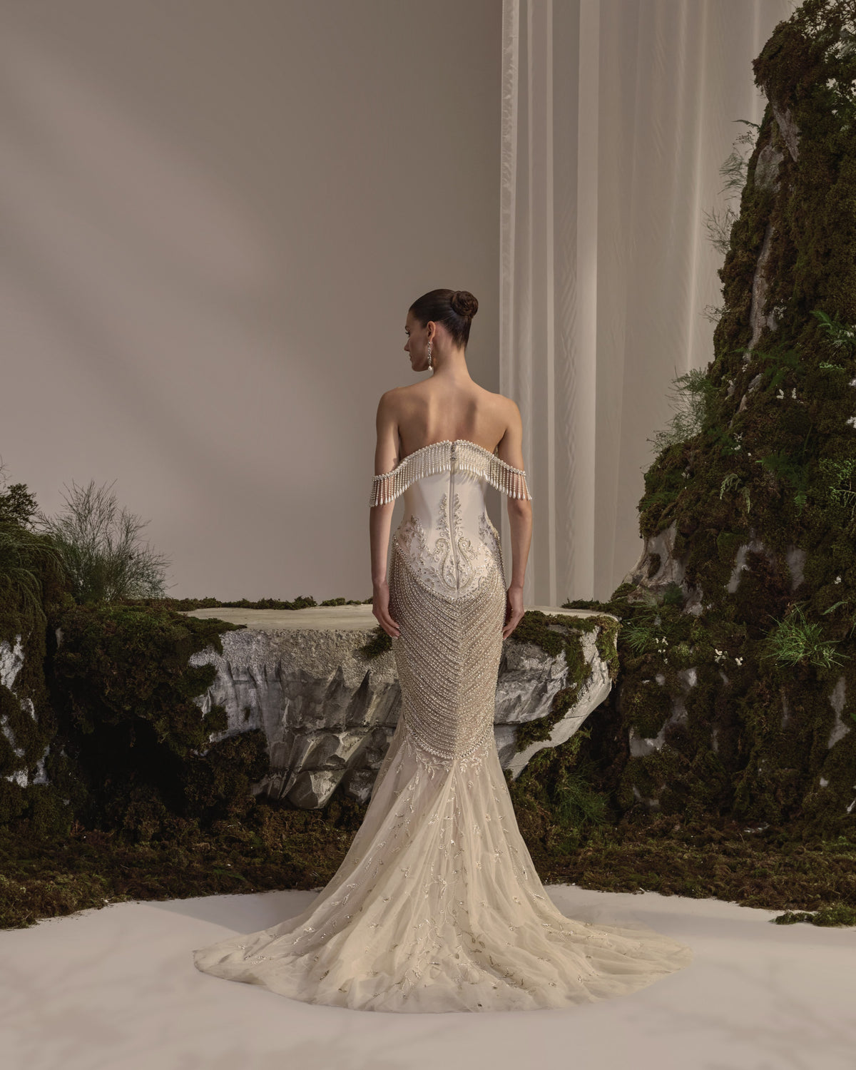 Off-shoulder bridal gown with a sculpted corset bodice, cascading bead embellishment, fitted embroidered skirt and sheer veil.