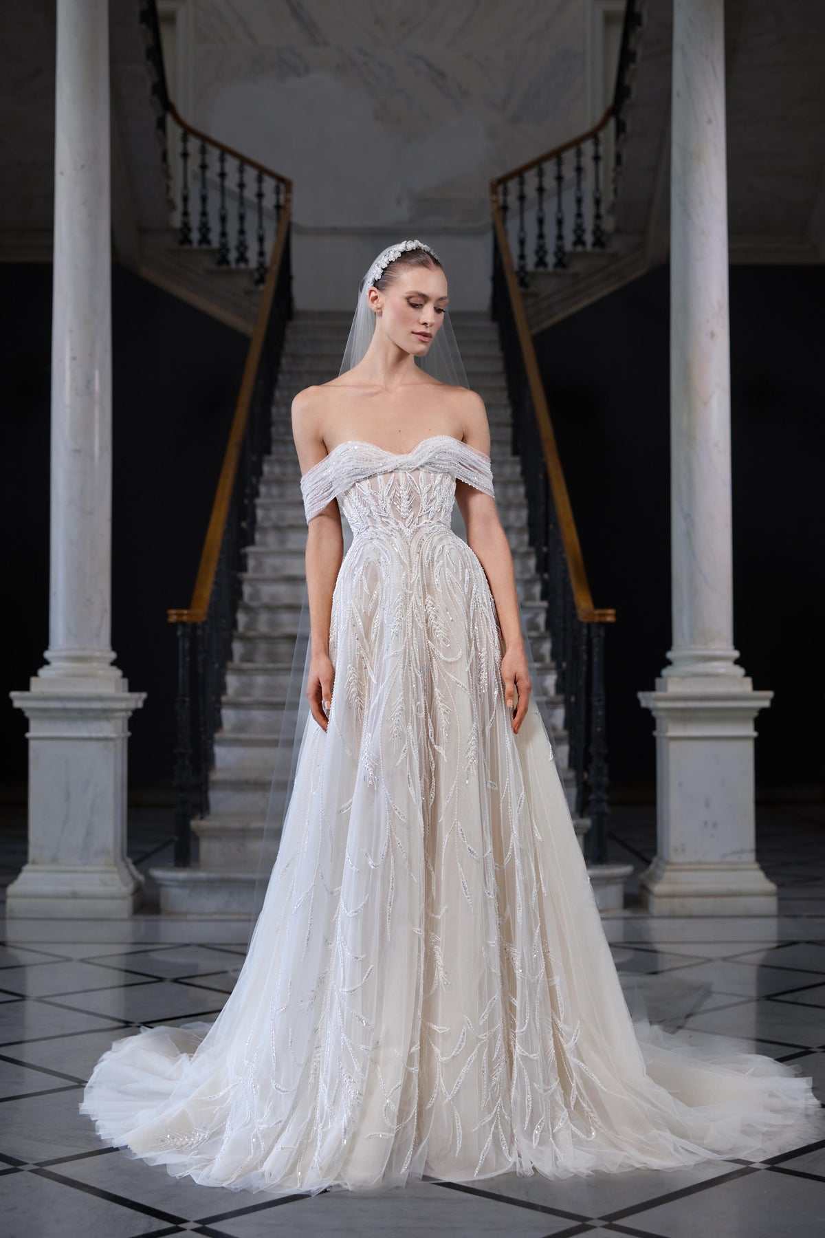 Off-shoulder bridal gown with a sculpted corset bodice, intricate beaded embroidery, flowing tulle skirt and sheer tulle veil.