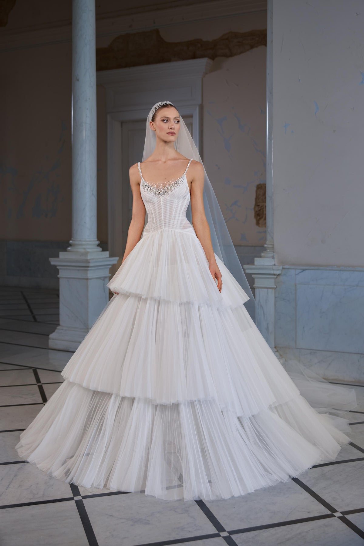 Bridal gown with a sheer corset bodice, embellished scoop neckline, delicate straps, voluminous tiered tulle skirt and sheer veil.