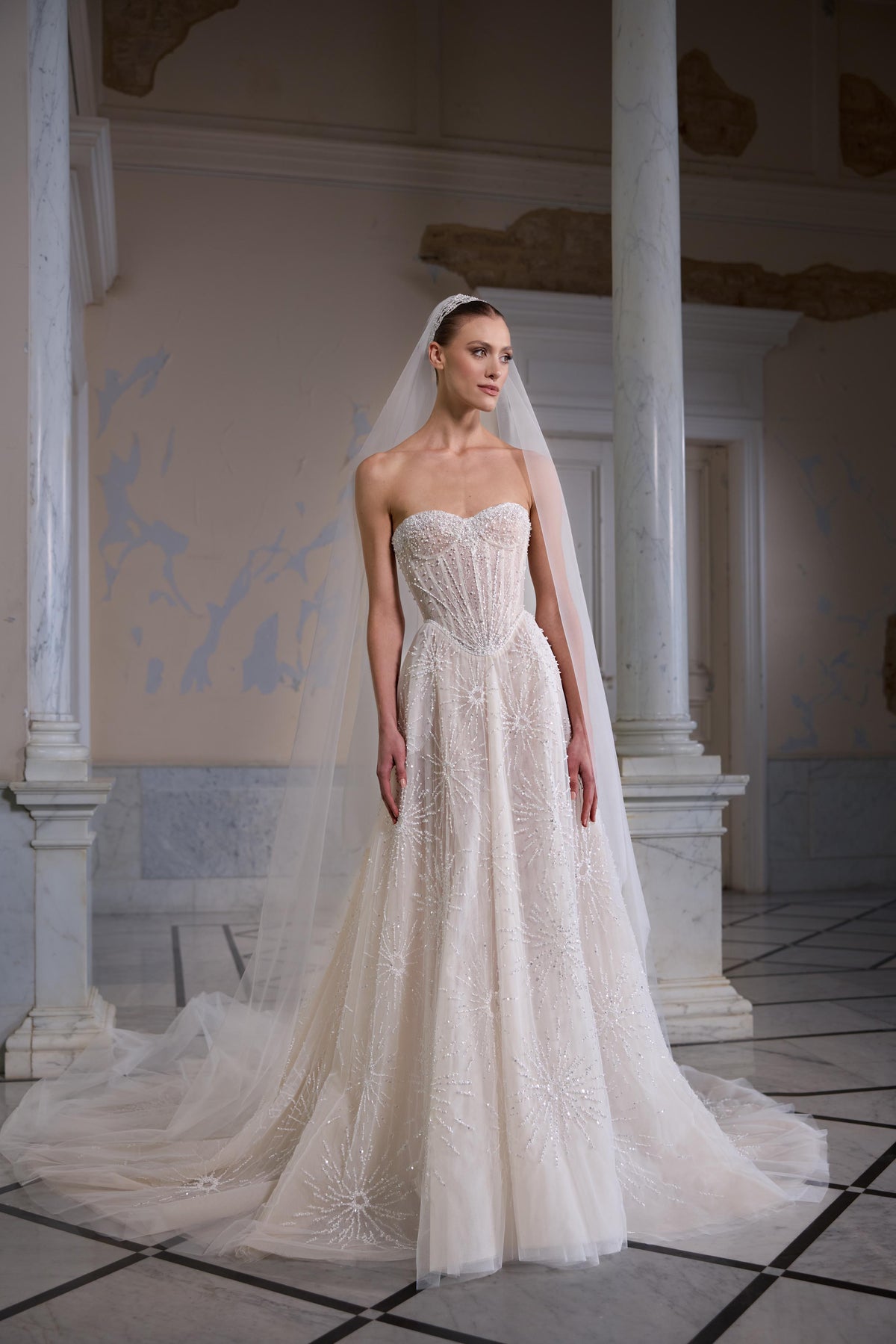 Strapless bridal gown with a sculpted corset bodice, radiant beaded embroidery, flowing tulle skirt and sheer tulle veil.