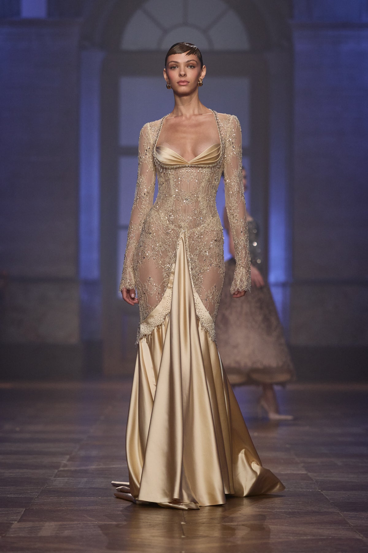 Champagne satin gown with a sheer crystal-embellished bodice, long sleeves and a flowing floor-length skirt.