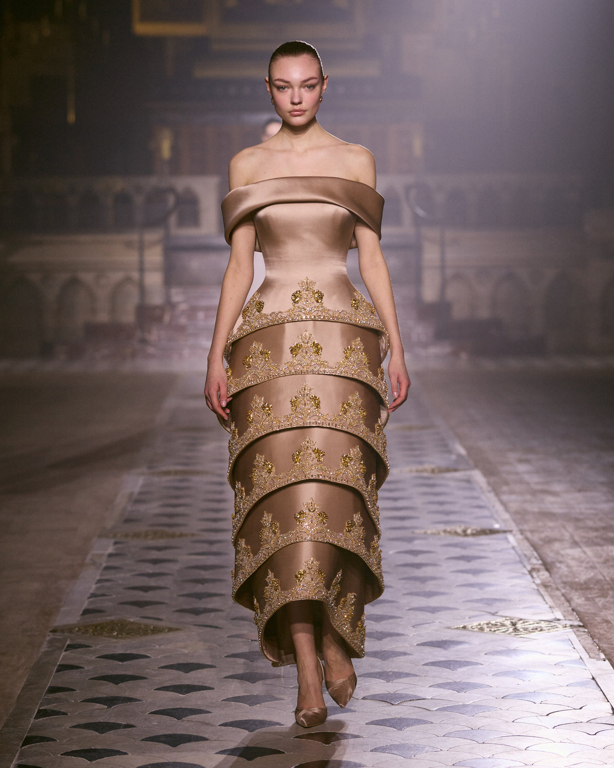 Bronze off-shoulder couture dress with sculpted tiered silhouette and intricate gold embellishment.