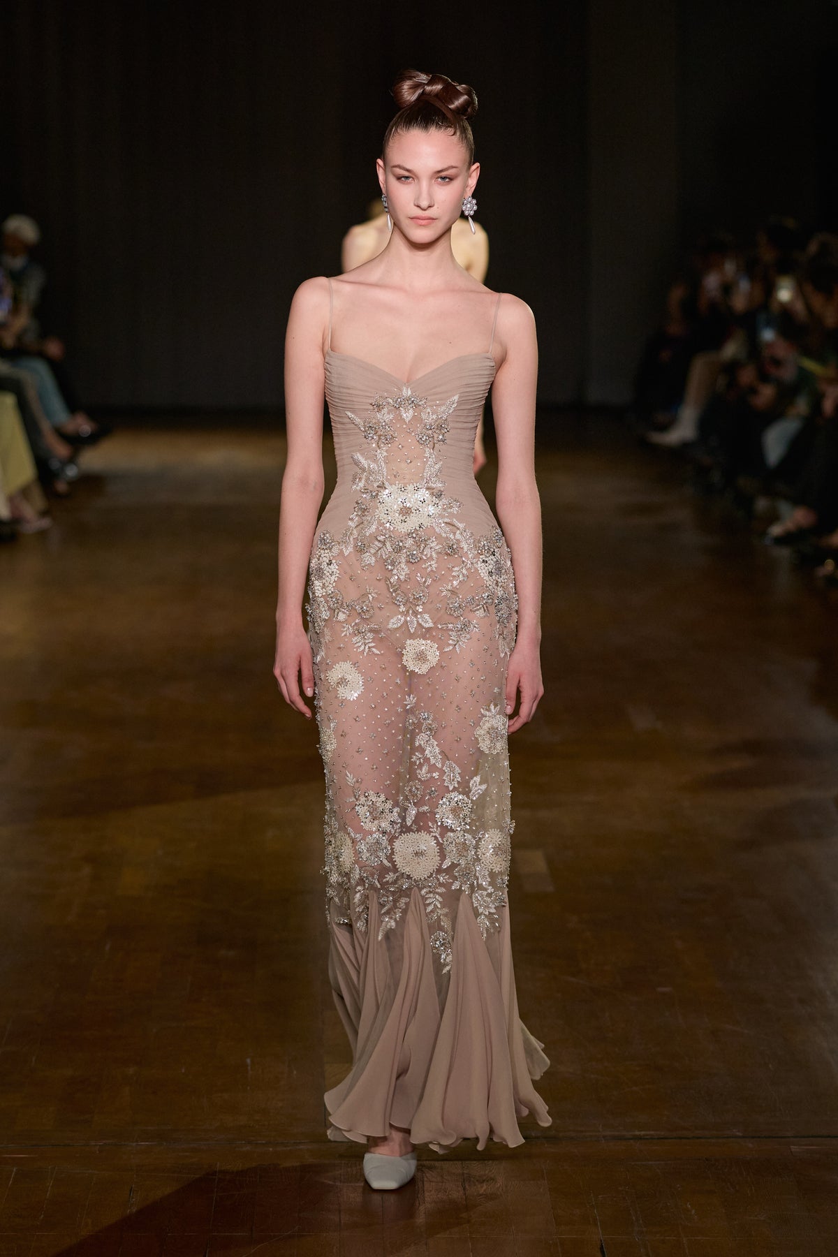 Nude tulle gown with draped bodice, thin straps, floral embroidery, crystal embellishments, and a fluid floor-length hem.