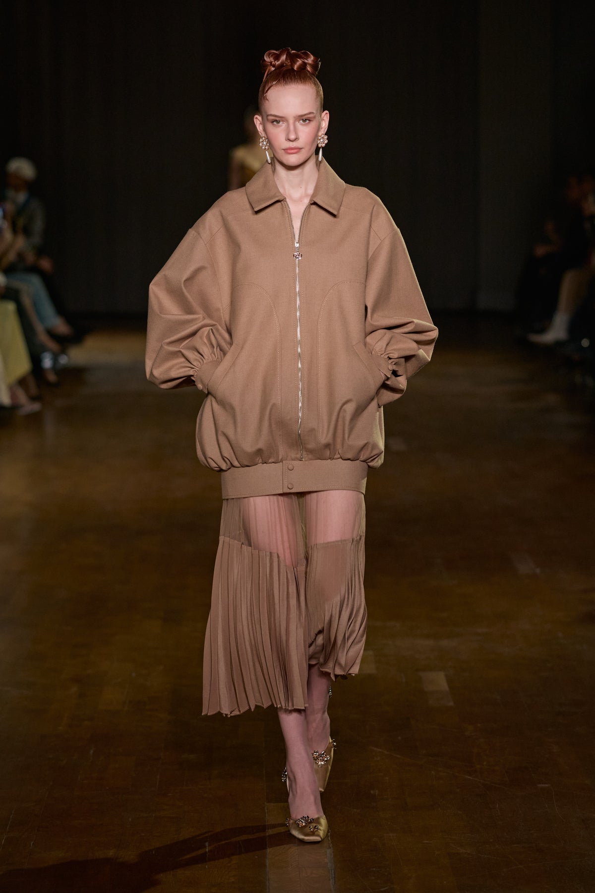 Taupe oversized zip-up jacket with voluminous sleeves paired with a sheer pleated tulle midi skirt.