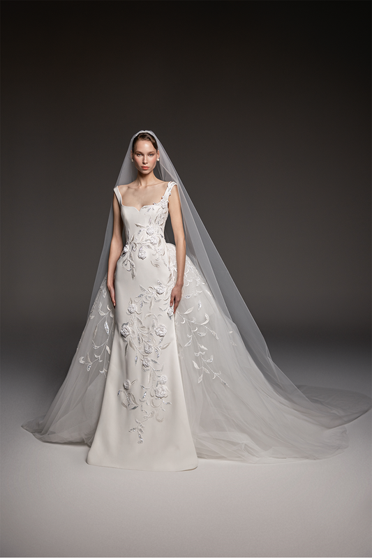 Sculpted bridal gown with floral embroidery, asymmetric shoulder detailing, a fitted silhouette and flowing tulle overskirt.