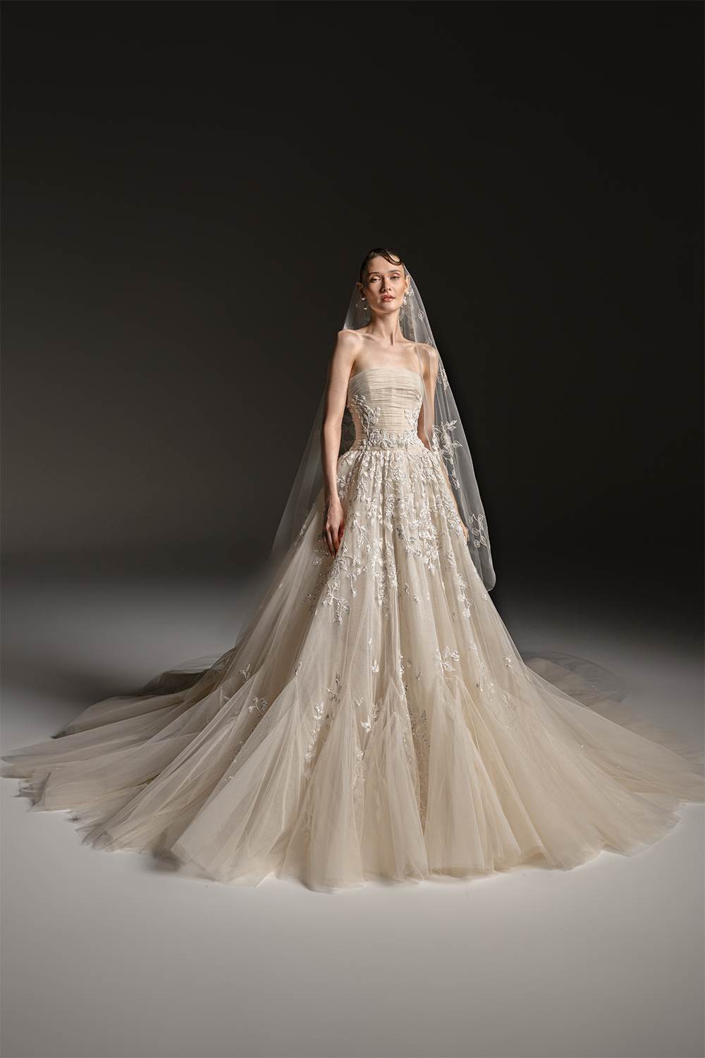 Strapless bridal gown in layered tulle with a draped bodice, floral embroidery and a voluminous floor-length skirt with train.