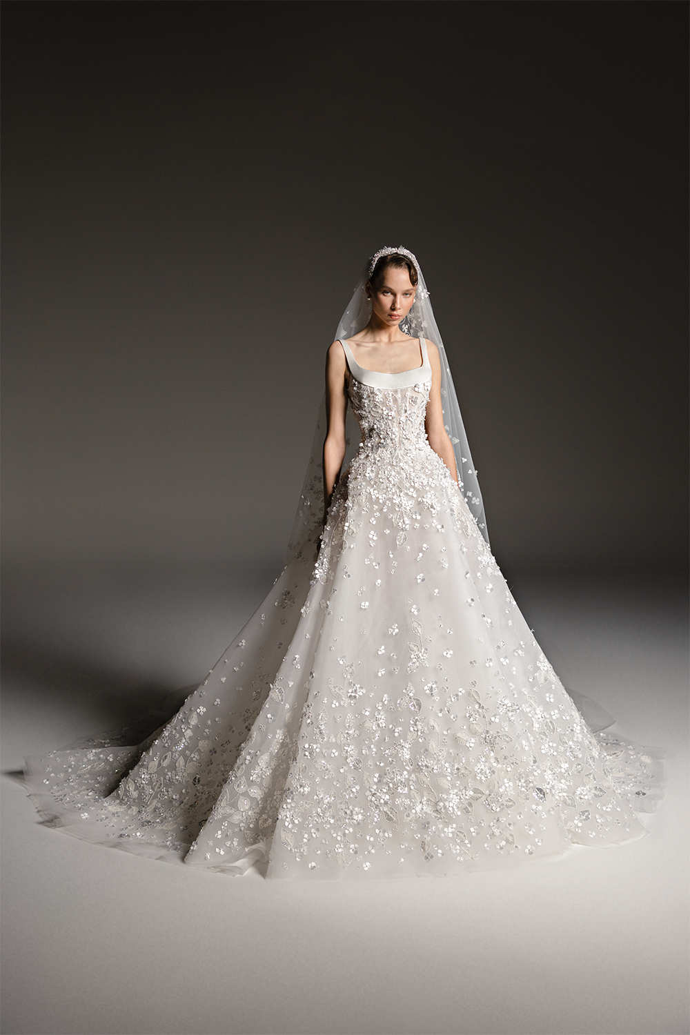 Bridal gown with a sculpted scoop-neck bodice, voluminous skirt and cascading three-dimensional floral embellishments.