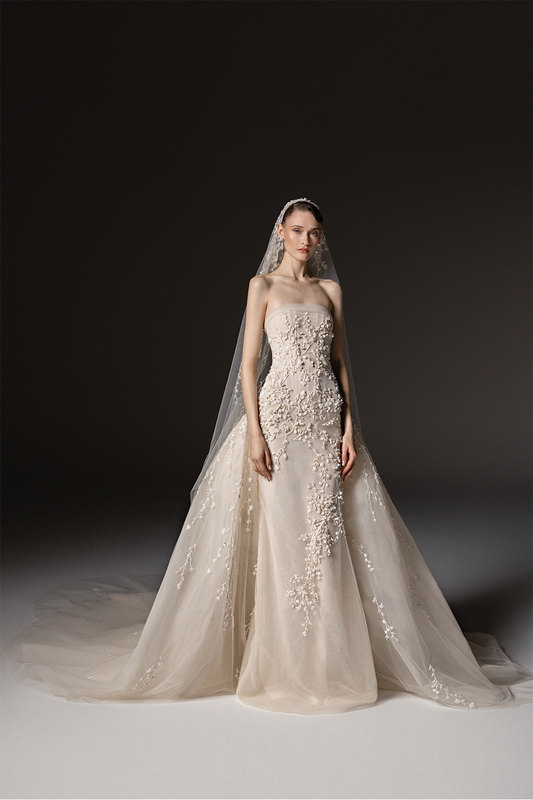 Strapless bridal gown in tulle with delicate botanical embroidery, a fitted silhouette and a voluminous embroidered overskirt.