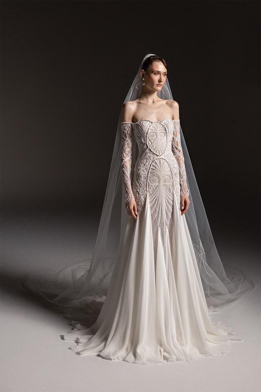 Off-shoulder bridal gown with sheer embroidered sleeves, an intricately beaded bodice and a flowing floor-length skirt.