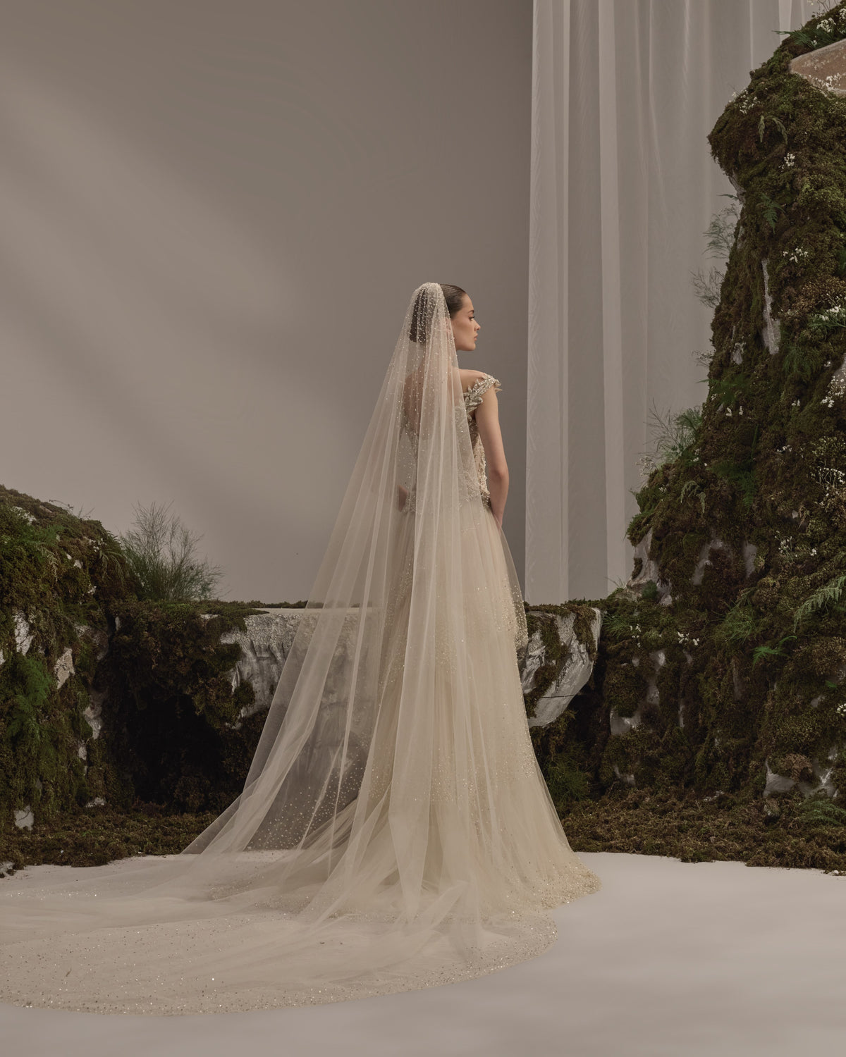 Bridal gown with an embellished sculpted corset bodice, delicate shoulder details, flowing beaded tulle skirt and sheer veil.