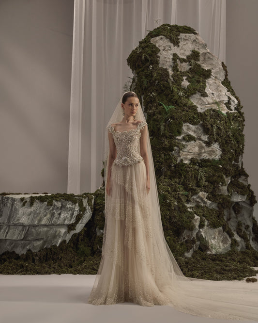 Bridal gown with an embellished sculpted corset bodice, delicate shoulder details, flowing beaded tulle skirt and sheer veil.