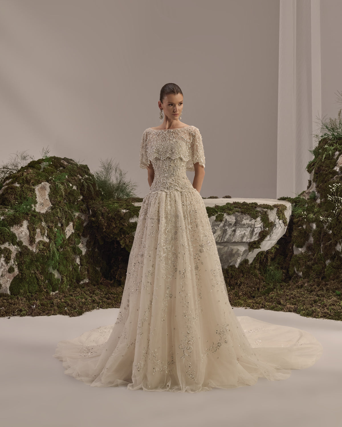 Bridal gown with a bateau neckline, short embellished sleeves, intricately embroidered bodice, fitted waist and flowing beaded tulle skirt with train.