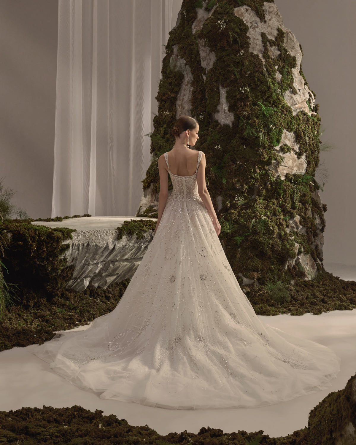 Bridal gown with delicate straps, a sculpted embellished corset bodice, flowing beaded tulle skirt and sheer veil.