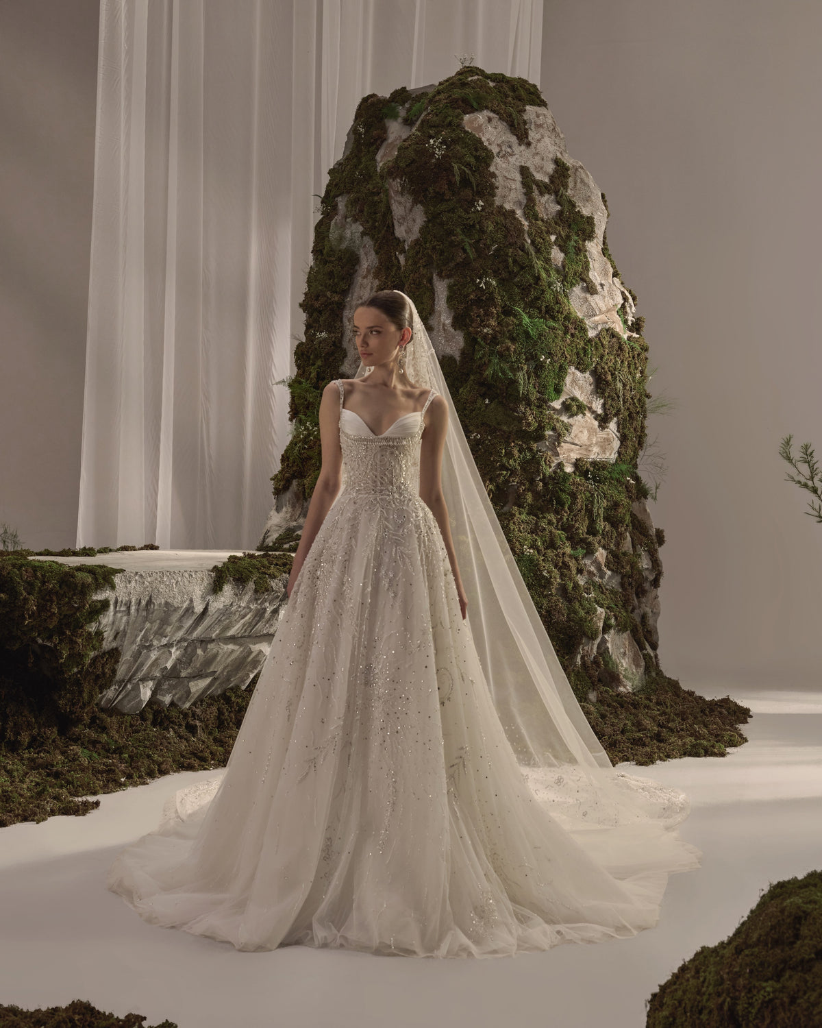 Bridal gown with delicate straps, a sculpted embellished corset bodice, flowing beaded tulle skirt and sheer veil.