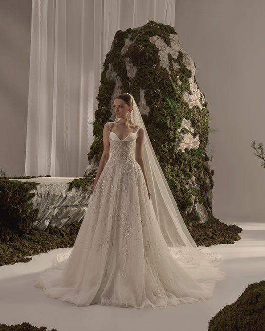 Bridal gown with delicate straps, a sculpted embellished corset bodice, flowing beaded tulle skirt and sheer veil.