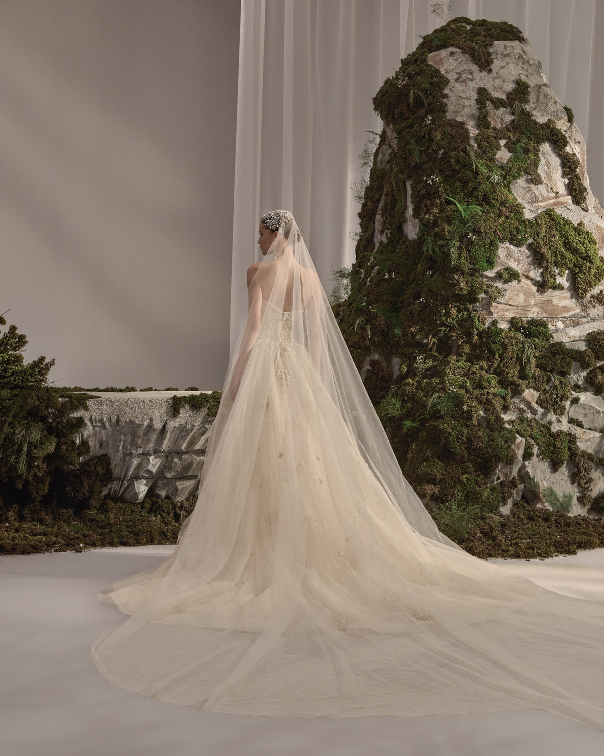 Strapless bridal gown with intricate embellishment, sculpted fitted silhouette, flowing tulle overskirt and sheer veil.