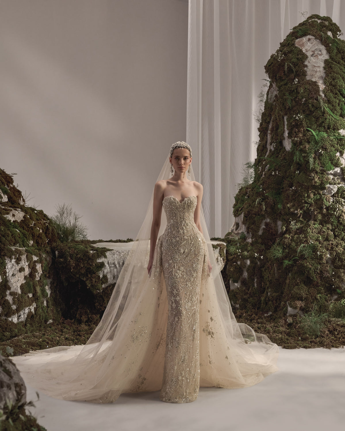 Strapless bridal gown with intricate embellishment, sculpted fitted silhouette, flowing tulle overskirt and sheer veil.
