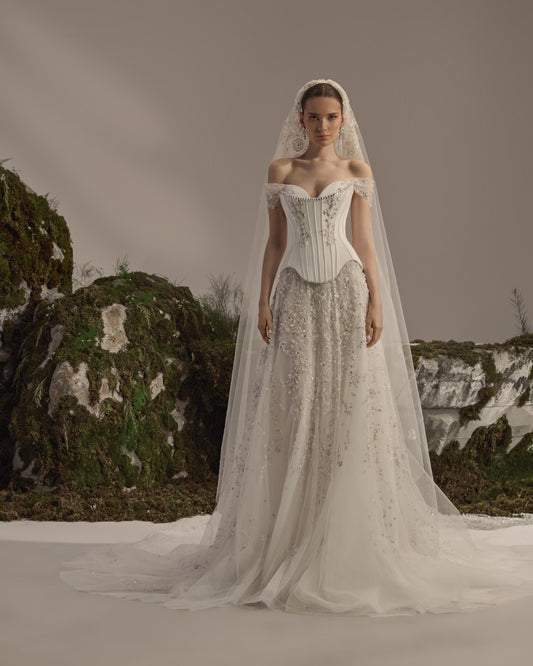 Off-shoulder bridal gown with a structured corset bodice, delicate embroidery, flowing tulle skirt and sheer veil.