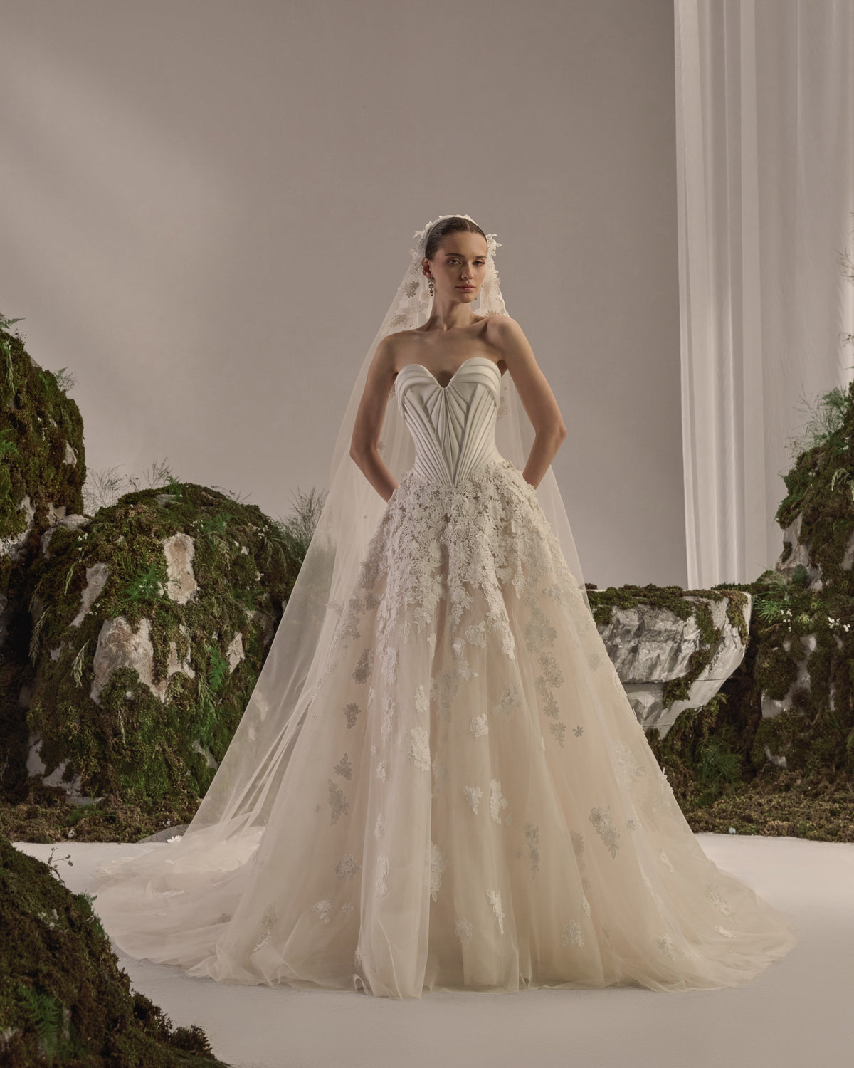 Strapless bridal gown with a sculpted corset bodice, voluminous tulle skirt, delicate lace appliqués and sheer veil.