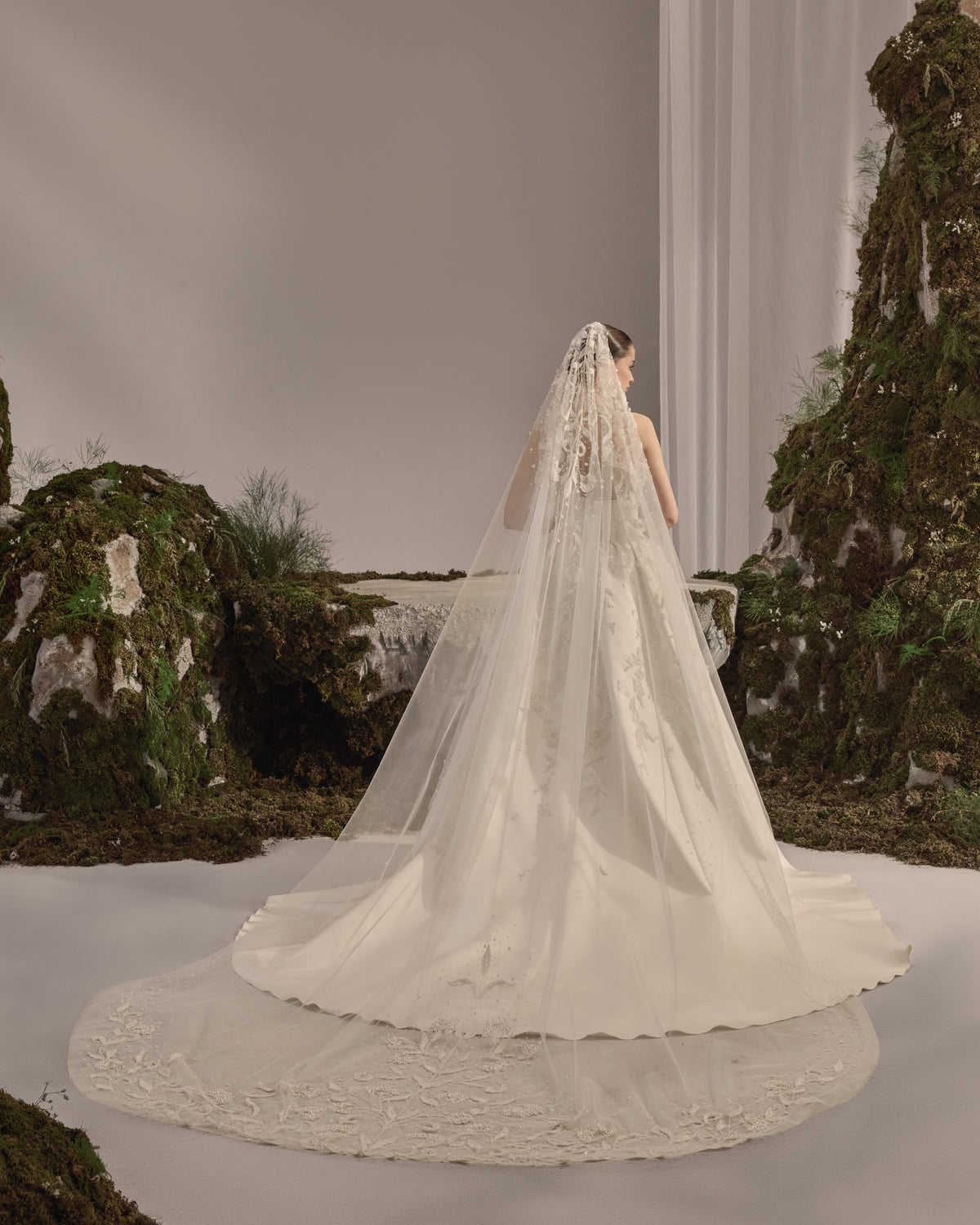 Strapless bridal gown with a structured embroidered bodice, voluminous satin skirt and sheer embellished veil.