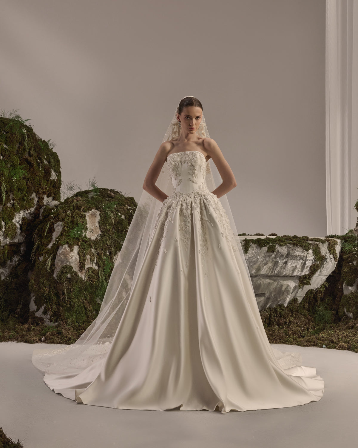 Strapless bridal gown with a structured embroidered bodice, voluminous satin skirt and sheer embellished veil.