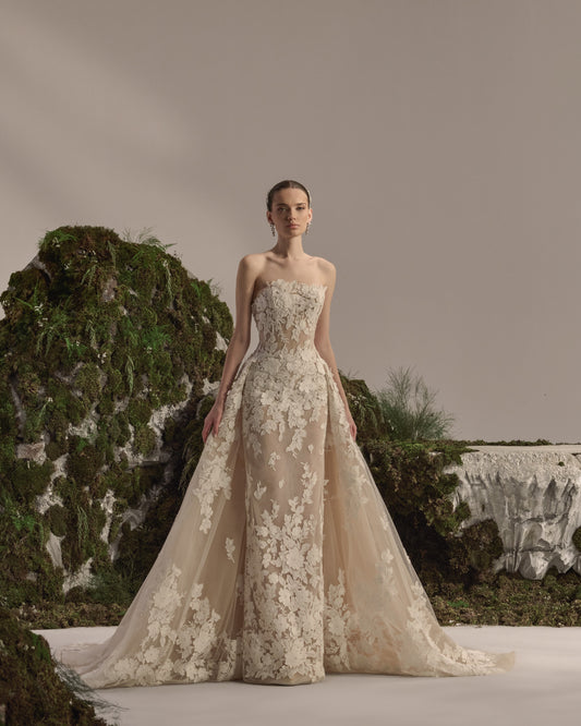 Strapless bridal gown with floral lace appliqués, sculpted fitted silhouette and a flowing lace overskirt.