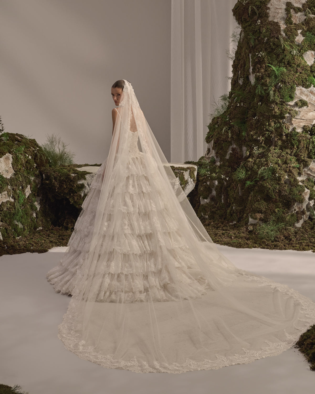 Bridal gown with a fitted lace corset bodice, delicate straps, button detailing, voluminous tiered lace skirt and sheer veil.