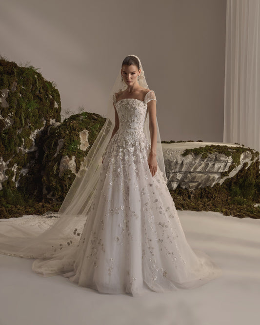 Bridal gown with a sculpted bodice, beaded cap sleeves, floral embellishment, flowing tulle skirt and sheer veil.