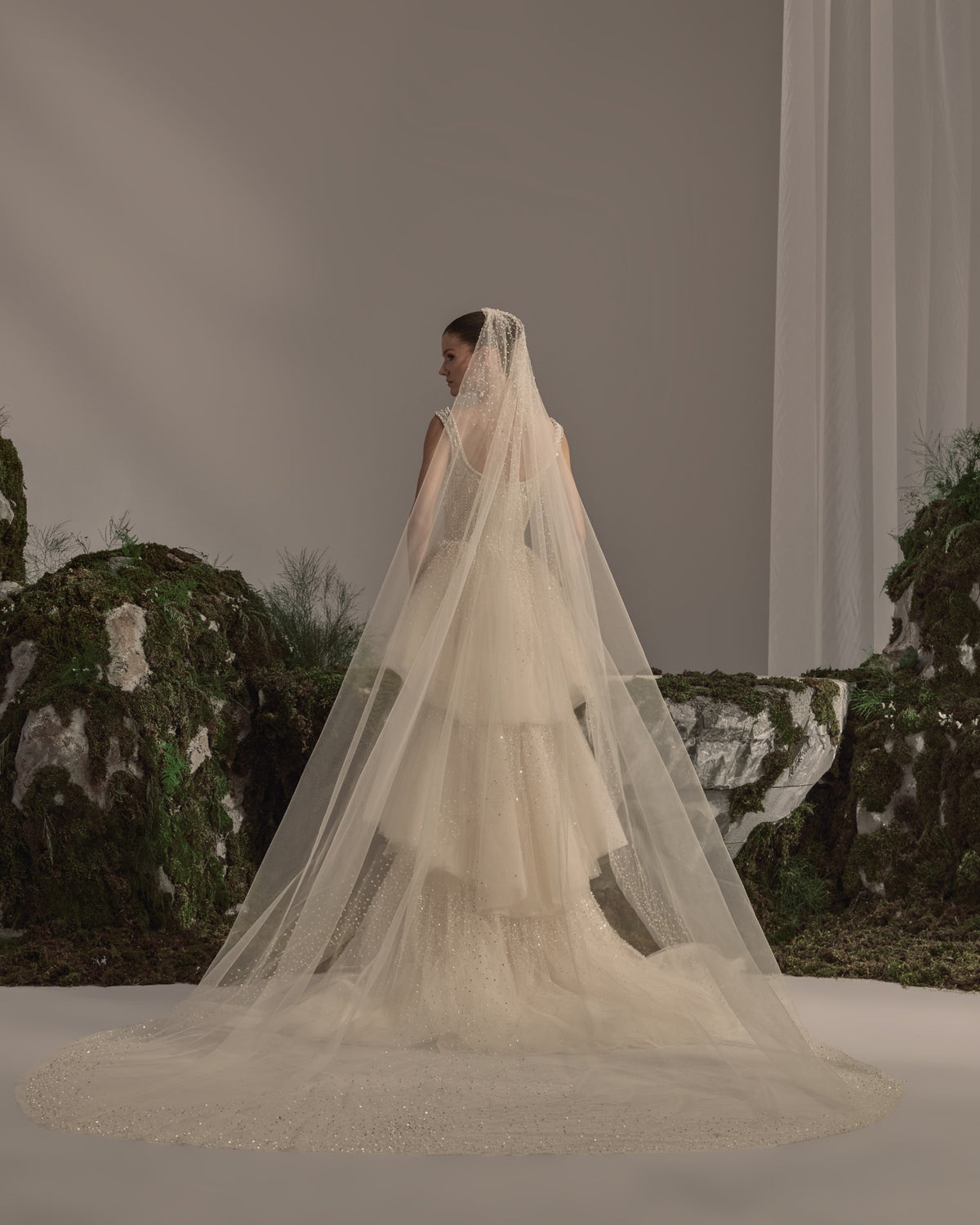 Bridal gown with an embellished square-neck bodice, delicate straps, tiered tulle skirt, shimmering details and a sheer veil.