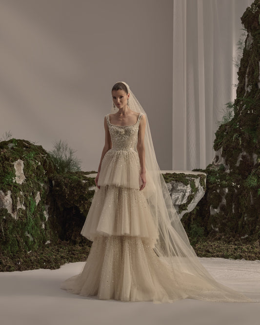 Bridal gown with an embellished square-neck bodice, delicate straps, tiered tulle skirt, shimmering details and a sheer veil.
