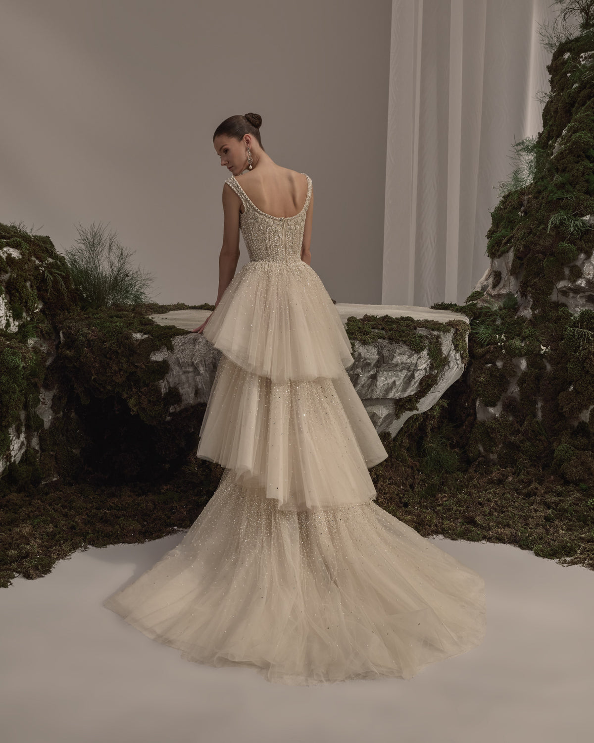 Bridal gown with an embellished square-neck bodice, delicate straps, tiered tulle skirt, shimmering details and a sheer veil.