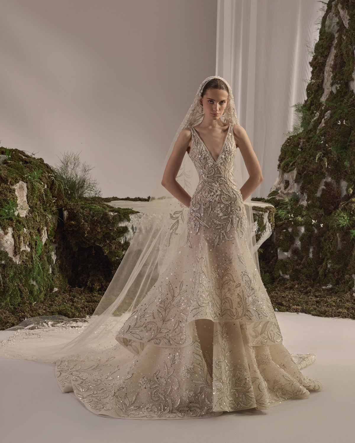 Bridal gown with an embellished sculpted corset bodice, delicate shoulder details, a flowing beaded tulle skirt, and a sheer veil.