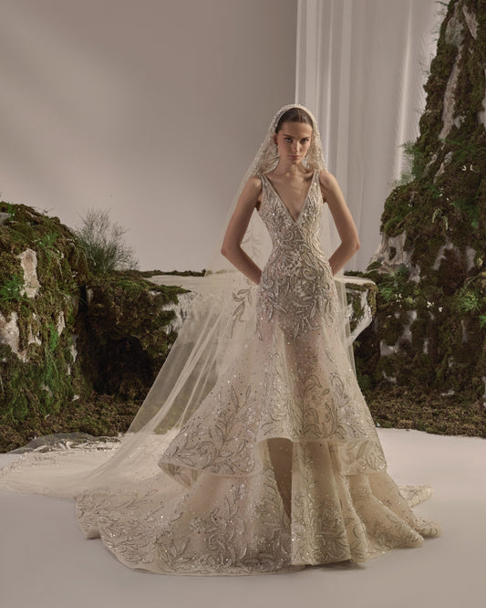 Bridal gown with an embellished sculpted corset bodice, delicate shoulder details, a flowing beaded tulle skirt, and a sheer veil.
