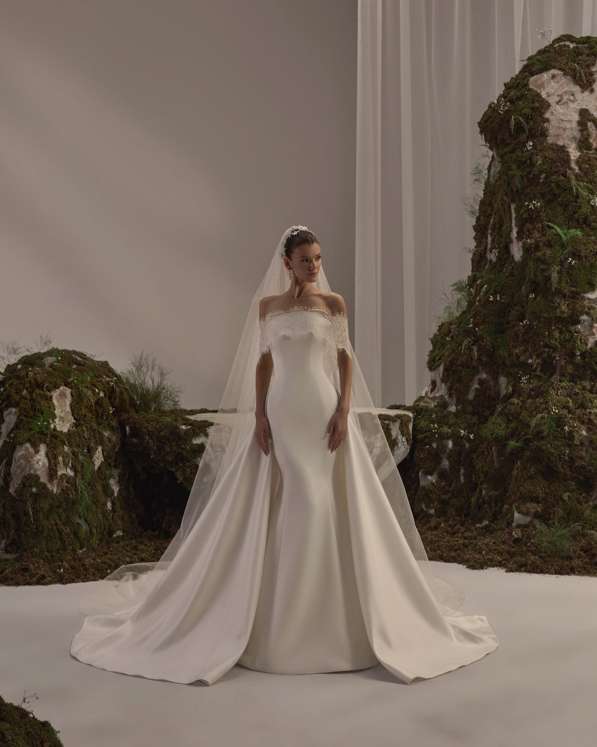 Off-shoulder bridal gown with delicate lace detailing, a fitted sculpted bodice and a flowing train with a sheer veil.