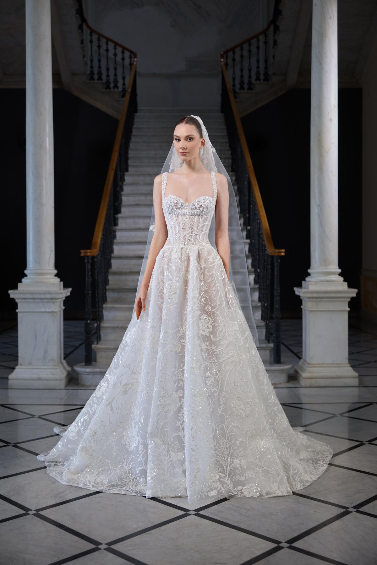 Bridal gown with a structured corset bodice, delicate straps, intricate floral embroidery, voluminous skirt and sheer veil.