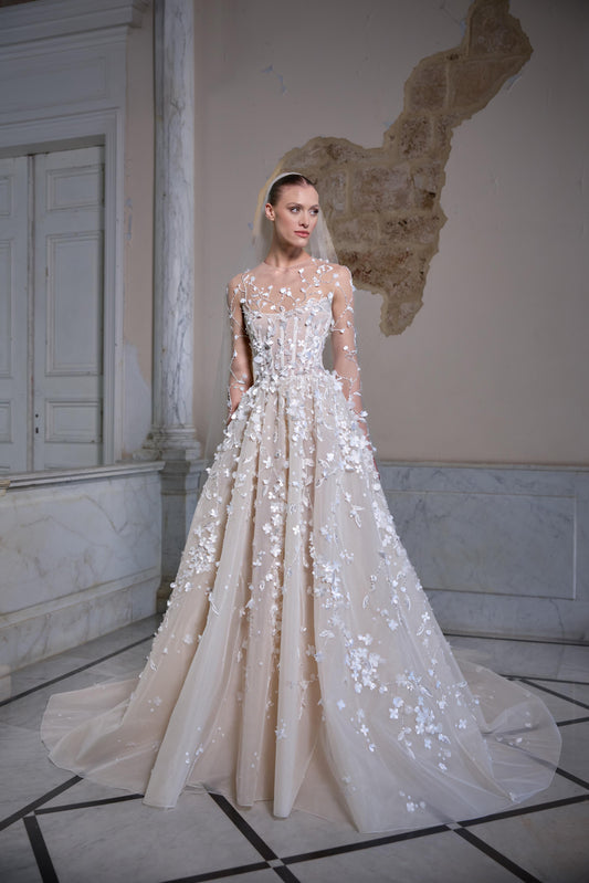 Bridal gown with a sheer corset bodice, long sheer sleeves, three-dimensional floral appliqués, voluminous tulle skirt and veil.