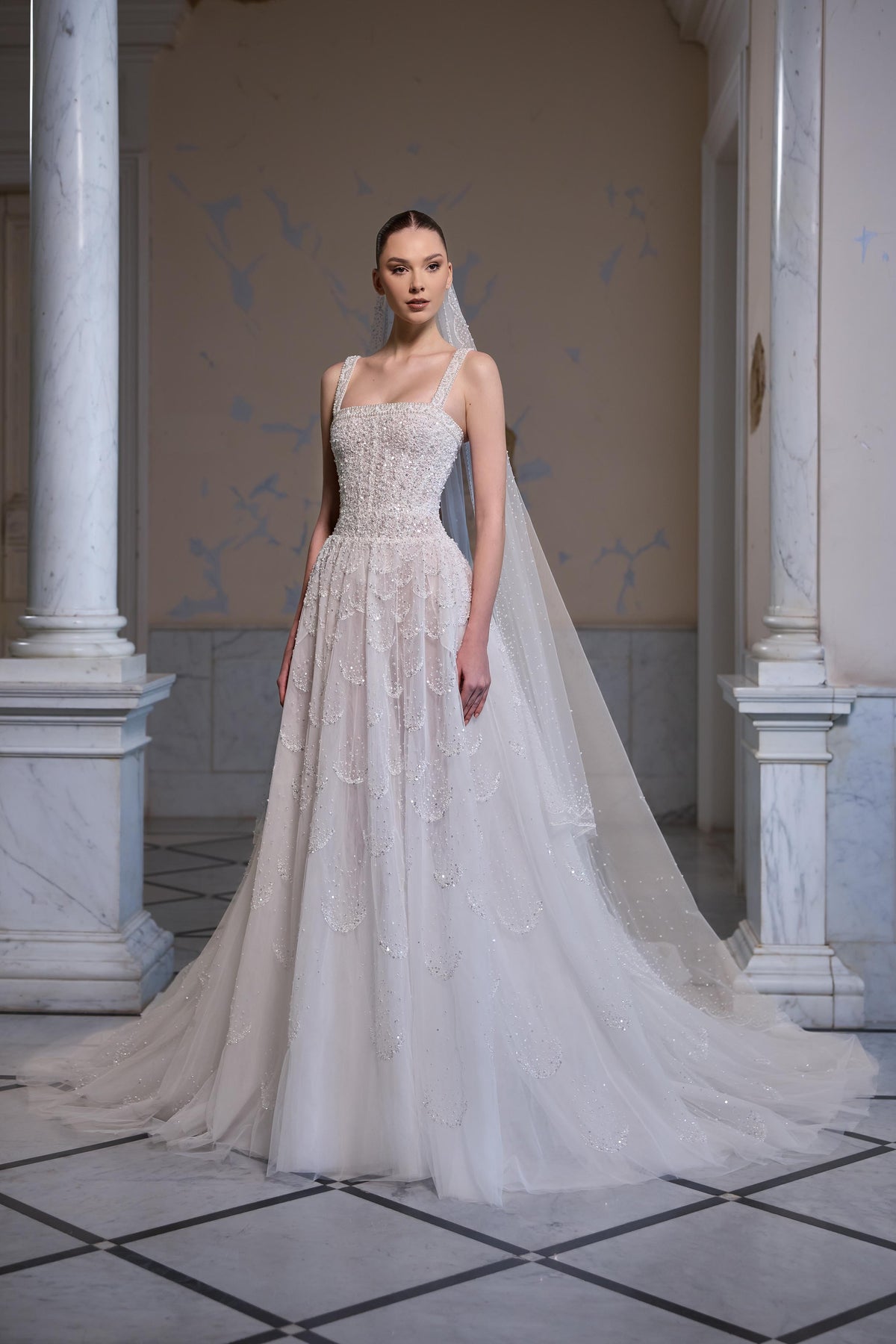 Square-neck bridal gown with an embellished fitted bodice, layered embroidered tulle skirt and sheer tulle veil.