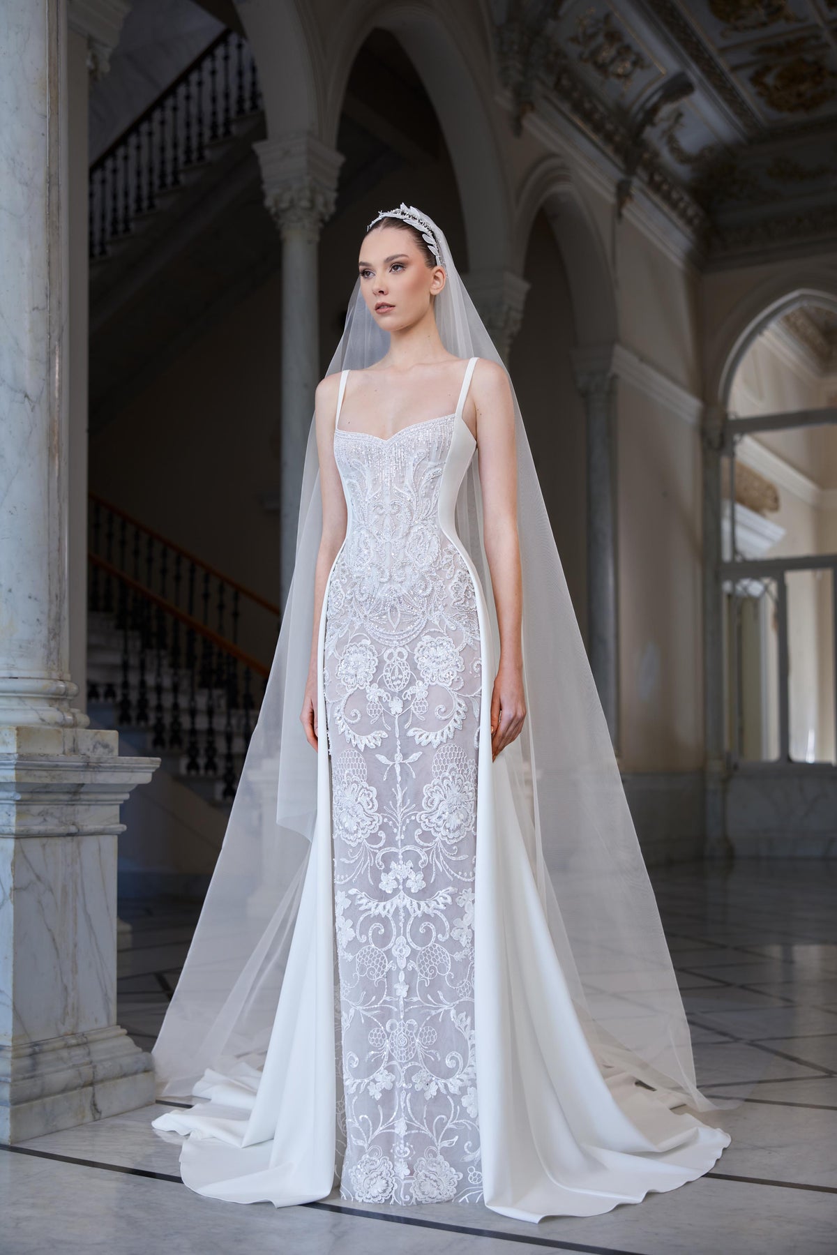 Fitted crêpe bridal gown with delicate straps, sheer embroidered front panel, sculpted silhouette, floor-length train and tulle veil.