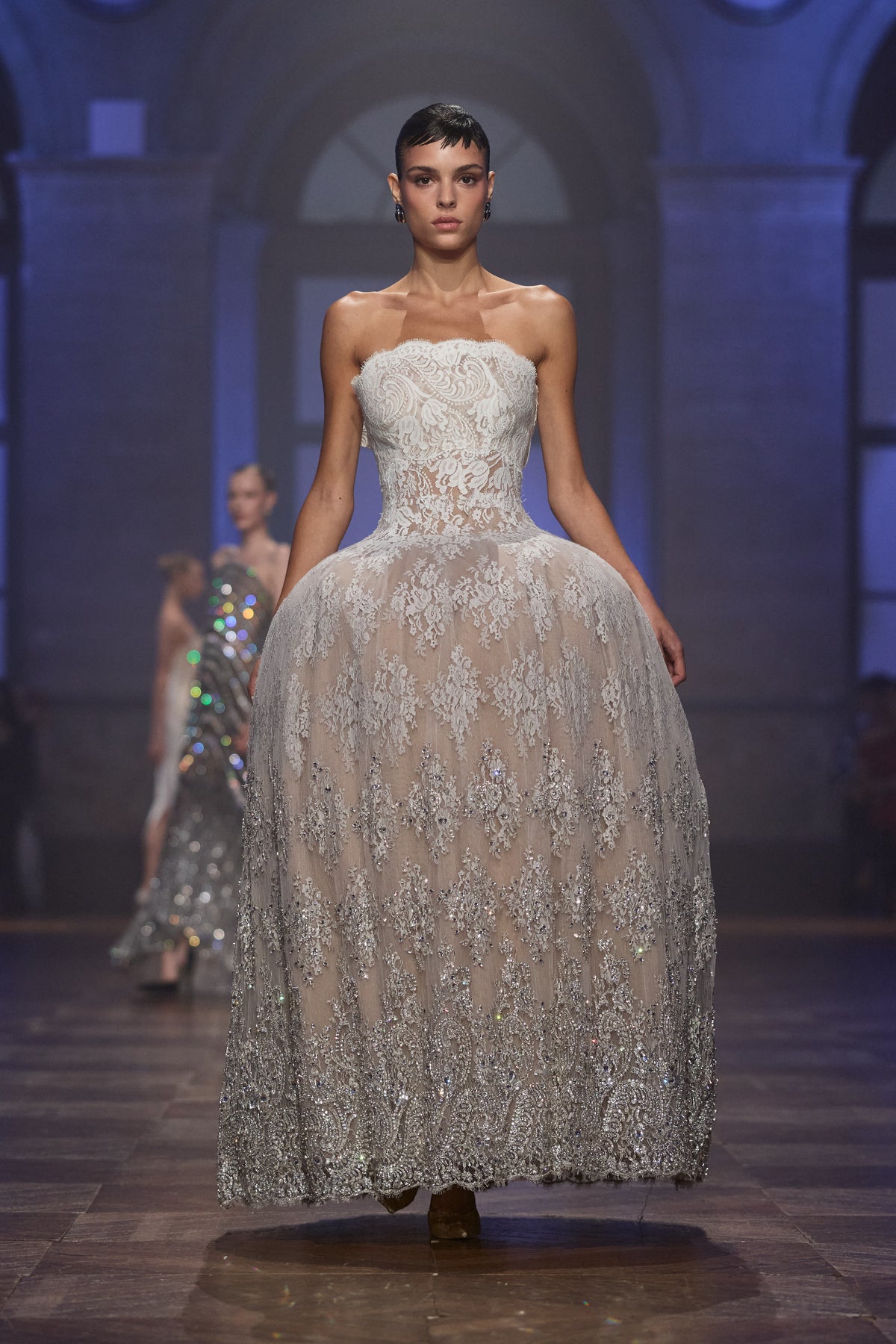 Ivory strapless couture gown with a sculpted silhouette, delicate lace and cascading silver crystal embellishments.
