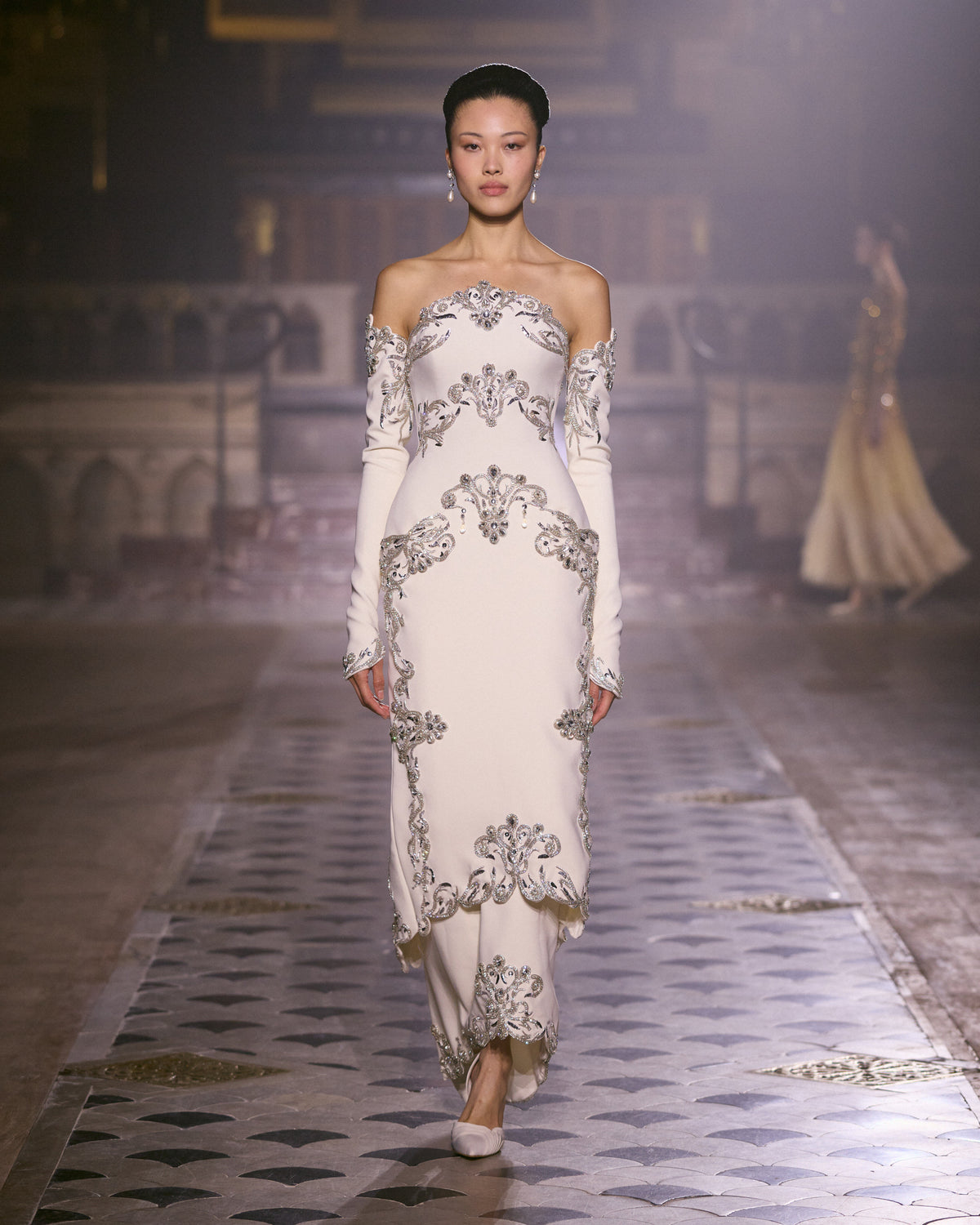 Ivory off-shoulder couture dress with long sleeves and intricate crystal embellishment.