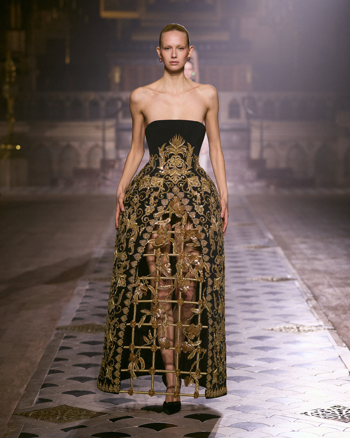 Strapless black couture gown with elaborate gold embroidery and sculptural openwork detailing along the skirt.
