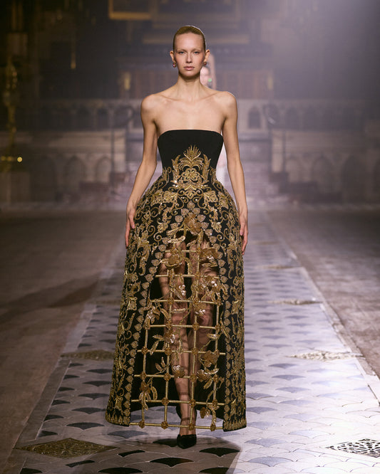Strapless black couture gown with elaborate gold embroidery and sculptural openwork detailing along the skirt.