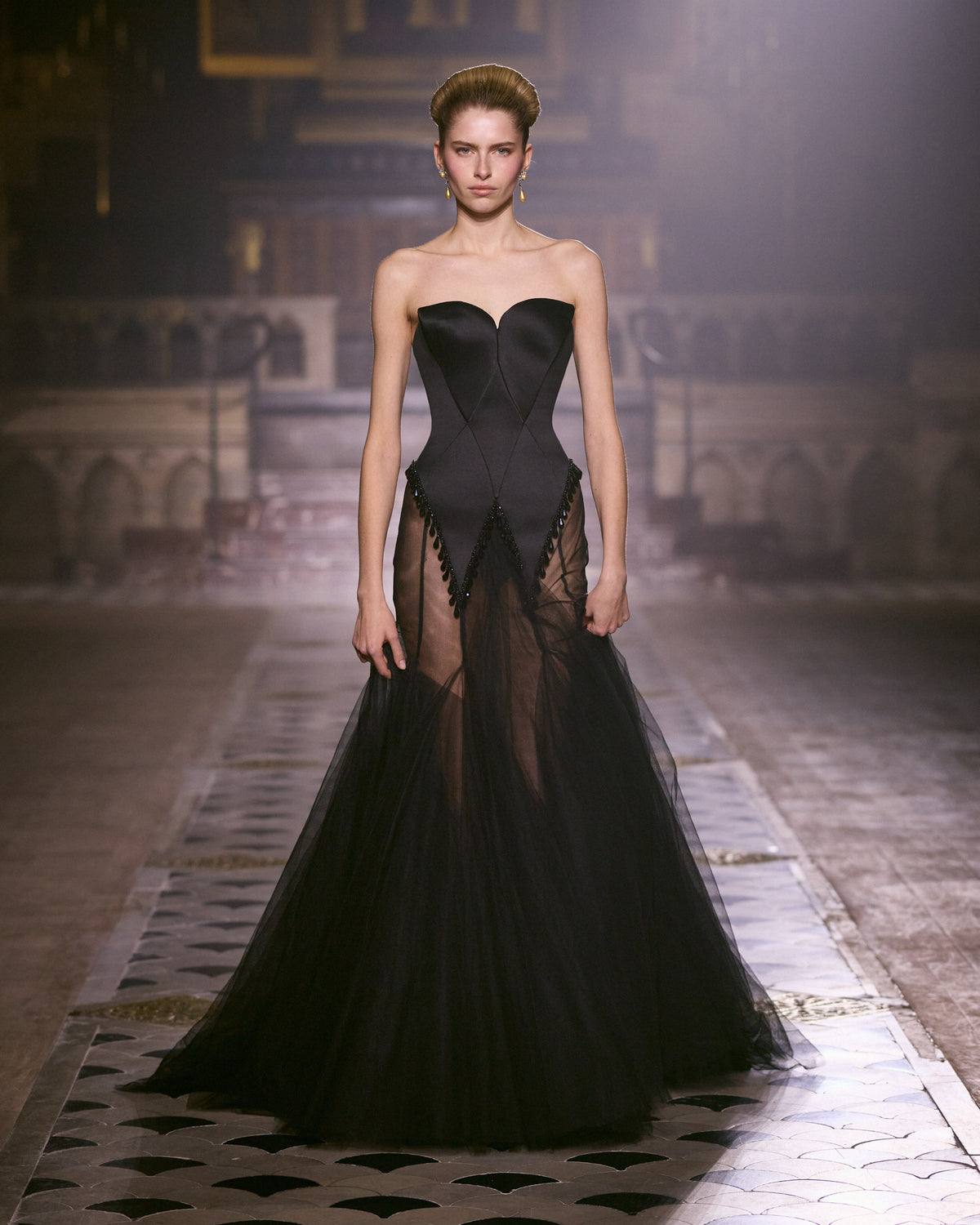 Black strapless couture gown with sculpted corset bodice, crystal-trimmed detailing and a sheer flowing tulle skirt.