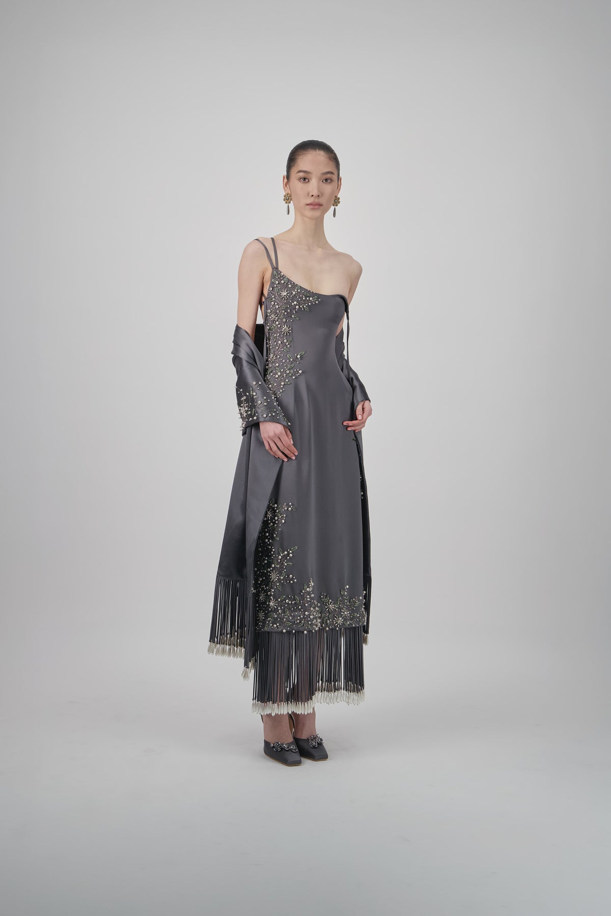 Satin shawl with intricate floral embellishments, draped construction and long statement fringe detailing.
Asymmetrical satin midi dress with slim straps, floral embellishments and a fluid silhouette with fringed hem detailing.
