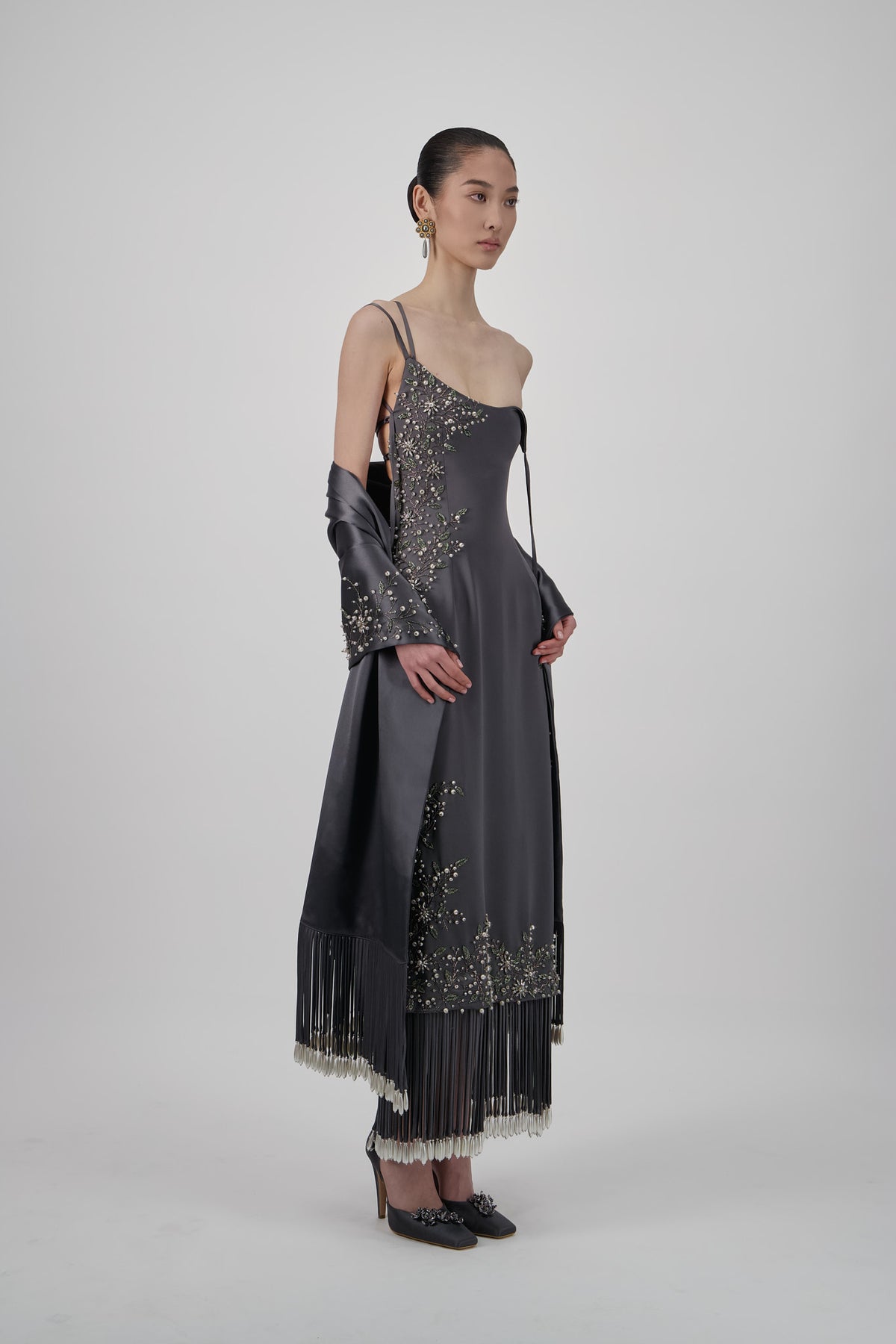 Satin shawl with intricate floral embellishments, draped construction and long statement fringe detailing.
Asymmetrical satin midi dress with slim straps, floral embellishments and a fluid silhouette with fringed hem detailing.