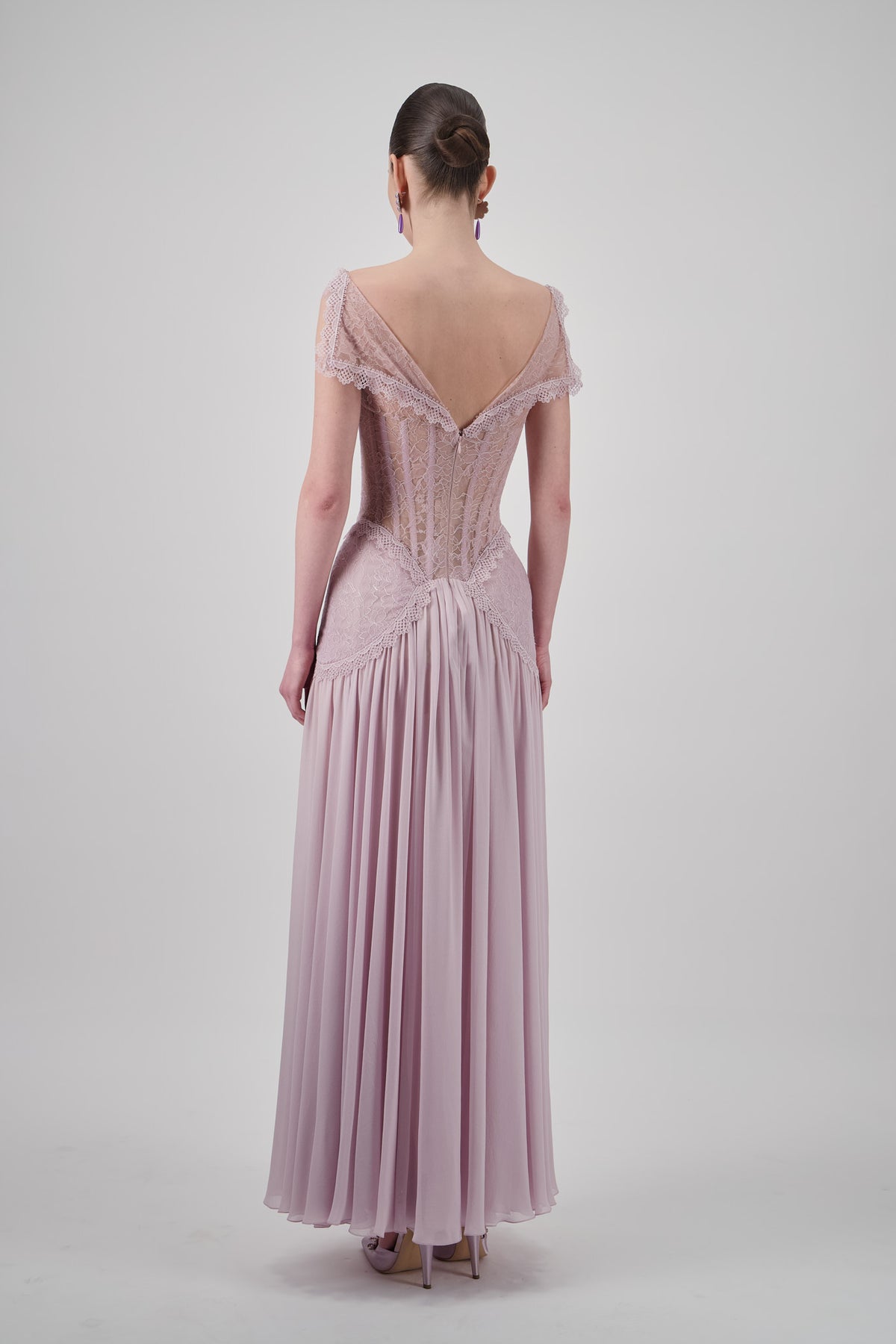 Pink lace long dress with sheer neckline, structured corset bodice, scalloped lace detailing and flowing pleated floor-length skirt.